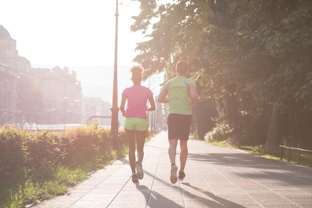 Gesundes junges multiethnisches Paar, das am frühen Morgen in der Stadt mit Sonnenaufgang im Hintergrund joggt