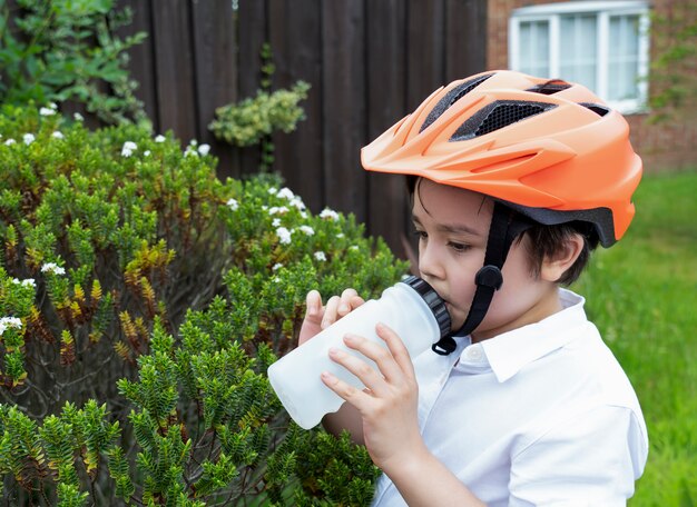 Gesundes Kind, das einen Fahrradhelm Trinkwasser trägt.