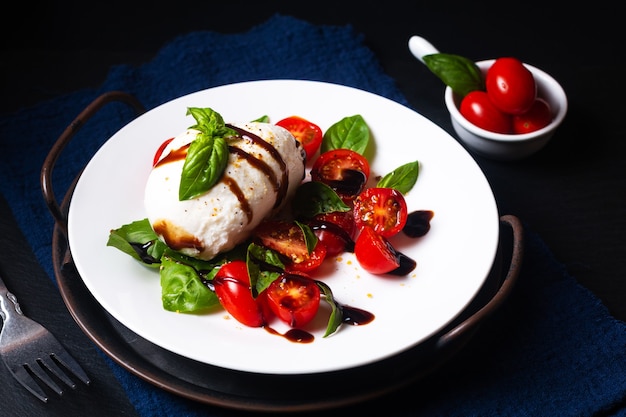 Gesundes Lebensmittelkonzept rustikaler Caprese-Salat auf schwarzem Hintergrund mit Kopienraum