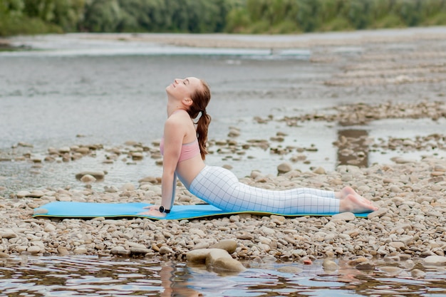Gesundes Mädchen, das sich entspannt, während es meditiert und Yogaübung in der schönen Natur am Ufer macht