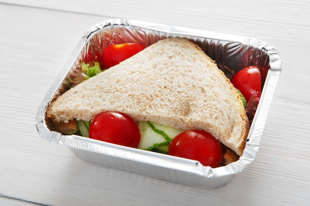 Foto gesundes mittagessen und diätkonzept. essen wegnehmen. sandwiches mit vollkornbrot, gurke und tomaten bei weißem holz