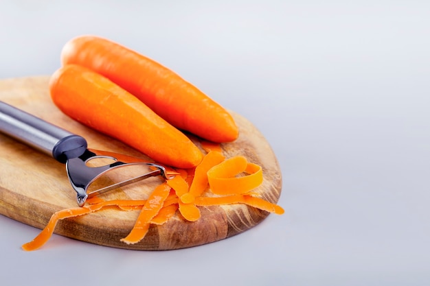 Gesundes Rohkost kochen. Karotten mit einem speziellen Messer schälen. Rohe Karotte auf Holzbrett auf grauem Hintergrund mit Kopienraum.