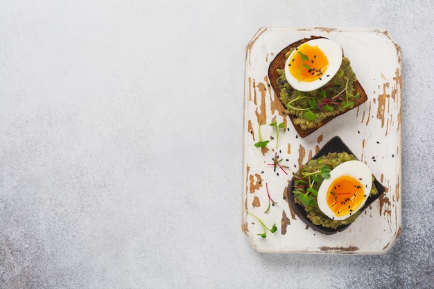 Gesundes Sandwich mit Avocado, Eiern und Microgreens auf Toast auf einem Servierteller zum Frühstück. Ernährungskonzept für gesunde Ernährung. Draufsicht.