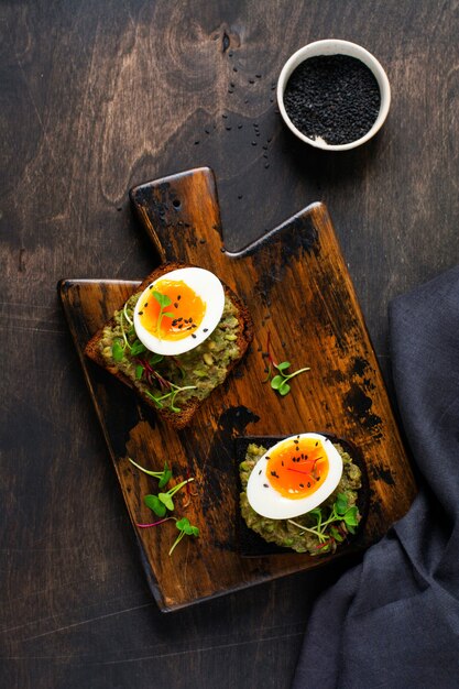 Gesundes Sandwich mit Avocado, Eiern und Microgreens auf Toast auf einer Servierplatte zum Frühstück. Ernährungskonzept für gesunde Ernährung. Ansicht von oben