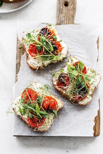 Gesundes Sandwich mit Frischkäse, gebackenen Tomaten und Mikrogemüse auf weißem Hintergrund