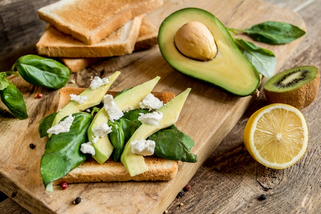 Gesundes Sandwich mit Käse und Avocado auf Holzbrett auf Laubhintergrund