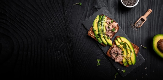 Gesundes Sandwich mit Thunfisch und geschnittener Avocado oben auf Holzhintergrund Draufsicht im langen Bannerformat