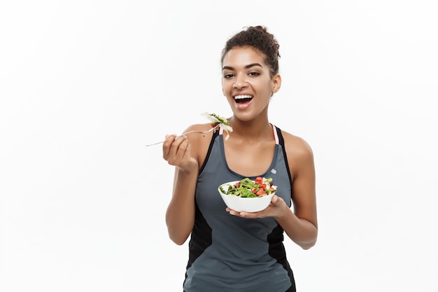 Gesundes und Eignungkonzept - schöne amerikanische afrikanische Dame in der Eignung kleidet auf der Diät, die frischen Salat isst.