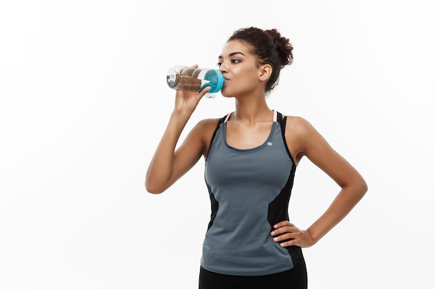 Gesundes und Fitness-Konzept schönes afroamerikanisches Mädchen in Sportkleidung Trinkwasser nach dem Training isoliert auf weißem Studiohintergrund