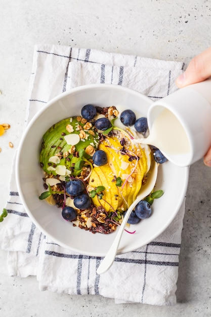 Foto gesundes veganes frühstück. granola mit avocado, superfoods, beeren und früchten in einer weißen schüssel, draufsicht.