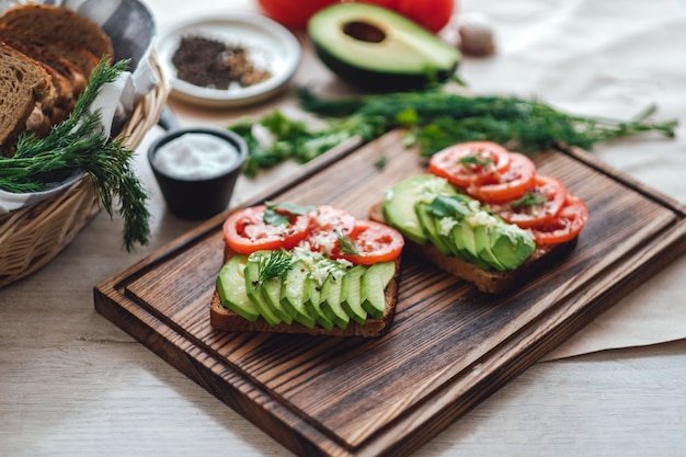 Gesundes veganes hausgemachtes Sandwich, Avocado und Tomaten mit dunklem Kornbrot auf einem Holzbrett.