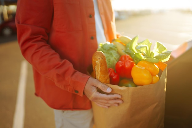 Gesundes veganes vegetarisches Essen in einer Papiertüte in den männlichen Händen Mann mit Einkaufstasche in der Nähe des Autos