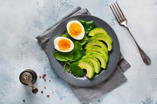 Gesundes vegetarisches Salatfrühstück. Spinatblätter, Tomate, Avocado und gekochtes Ei auf grauem Teller und altem grauem Betonhintergrund. Buddha-Schale. Draufsicht.