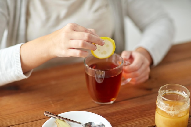 Gesundheit, traditionelle Medizin und Ethnoscience Konzept - Nahaufnahme einer kranken Frau, die Tee mit Zitrone, Honig und Ingwer an einem Holztisch trinkt