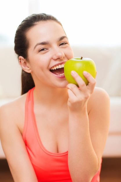 Gesundheits-, Diät-, Heim- und Glückskonzept - lächelnde sportliche Teenagerin mit grünem Apfel zu Hause