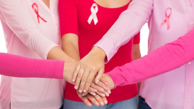 Foto gesundheits-, menschen-, gesten- und medizinkonzept - nahaufnahme von frauen in leeren hemden mit rosa brustkrebs-aufklärungsbändern, die die hände auf den weißen hintergrund legen