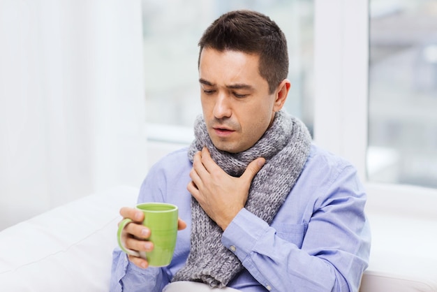 Gesundheits-, Menschen- und Medizinkonzept - kranker Mann mit Grippehusten und heißem Tee aus der Tasse zu Hause trinken