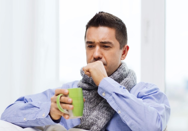 Gesundheits-, Menschen- und Medizinkonzept - kranker Mann mit Grippehusten und heißem Tee aus der Tasse zu Hause trinken