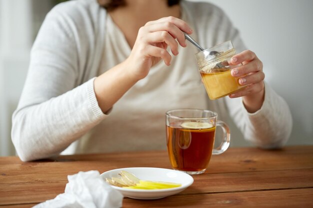 Foto gesundheits-, traditionelle medizin- und ethnowissenschaftskonzept - nahaufnahme einer frau, die honig zum tee mit zitrone hinzufügt