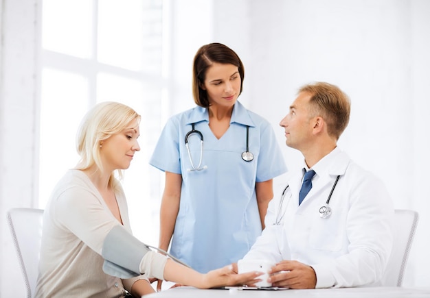 Gesundheits- und medizinisches Konzept - Arzt und Krankenschwester mit Patienten, die den Blutdruck messen