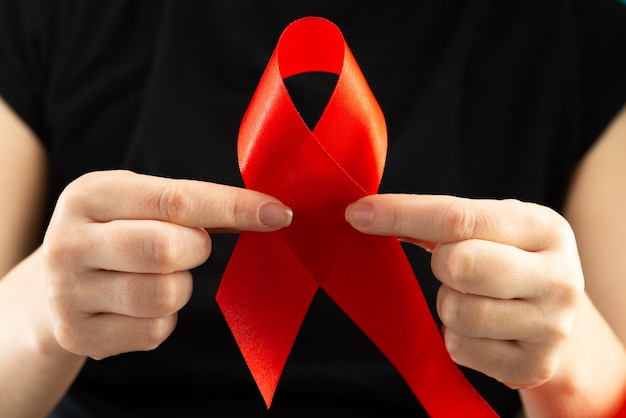 Gesundheits- und Medizinkonzept. AIDS-Bewusstsein. Weibliche Hände halten rotes AIDS-Bewusstseinsband. Welt-AIDS-Tag