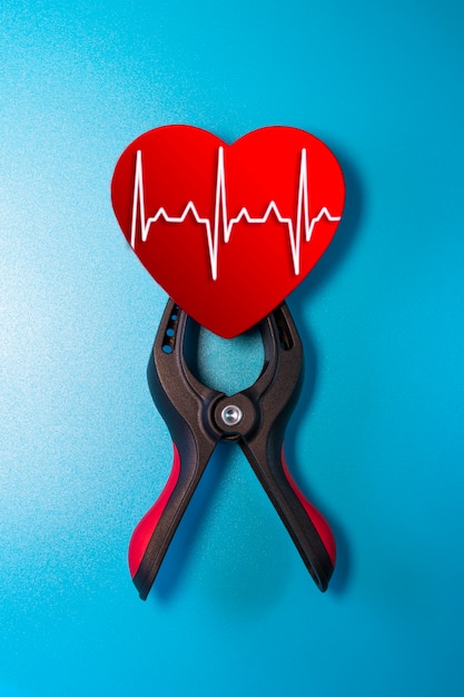 Gesundheits- und Medizinkonzept - Nahaufnahme eines roten Herzens mit einer EKG-Linie, die in einem Schraubstock zur Wiederbelebung eingeklemmt ist. Rettung des Lebens und der Gefühle. Valentinstag.
