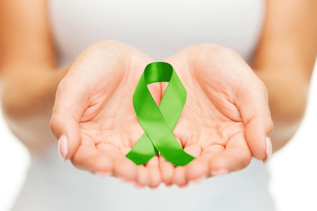 Gesundheits- und Medizinkonzept - weibliche Hände, die ein grünes Bewusstseinsband für Organtransplantationen halten
