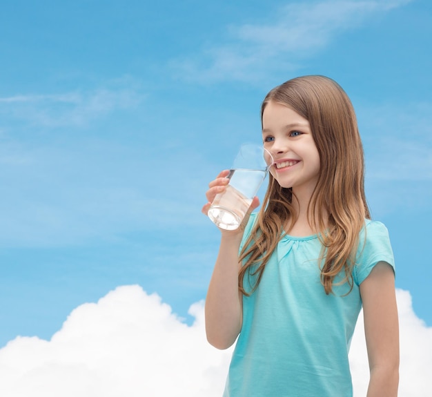 Gesundheits- und Schönheitskonzept - lächelndes kleines Mädchen mit Glas Wasser