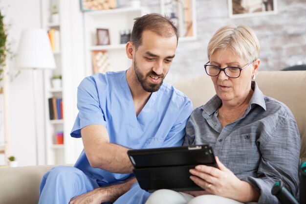 Gesundheitsbesucherin hilft Seniorin bei der Nutzung von Tablets im Pflegeheim.