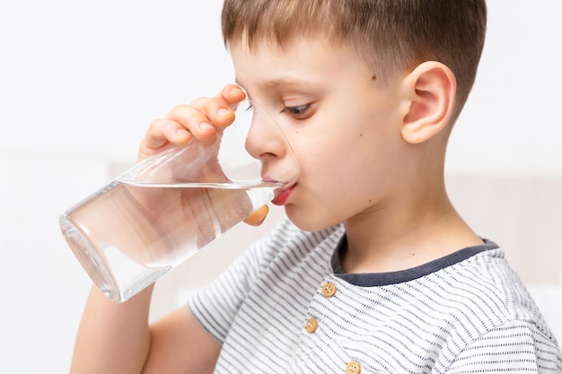 Gesundheitskonzept Kind trinkt morgens frisches, reines Wasser aus einem Glas, das sich auf dem Bett befindet Kümmert sich um Ihren Körper Erwachensritual Nahaufnahme