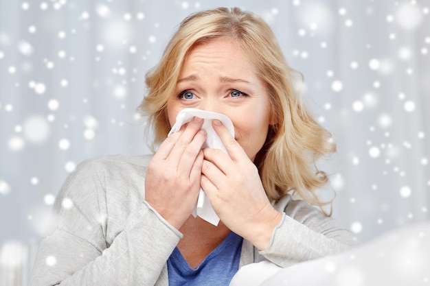 Gesundheitsversorgung, Grippe, Hygiene und Menschenkonzept - kranke Frau, die ihre Nase auf eine Papier Serviette über Schnee bläst