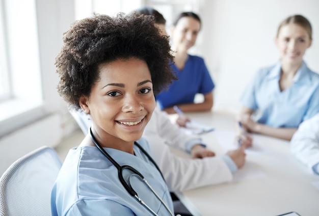 gesundheitswesen, beruf, menschen und medizinkonzept - glückliche afroamerikanische ärztin oder krankenschwester über einer gruppe von medizinern, die sich im krankenhaus treffen