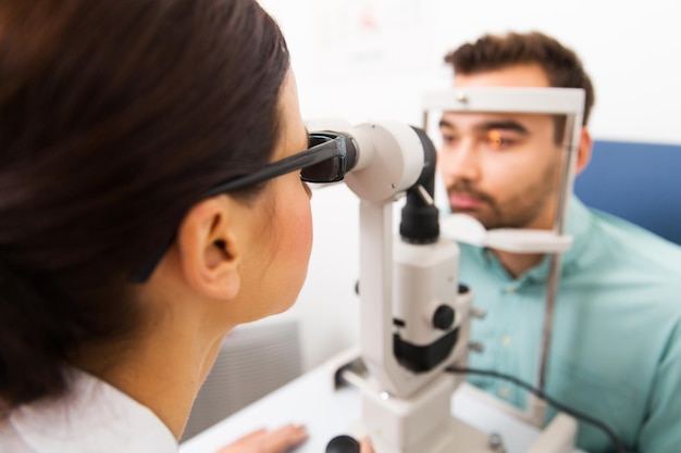 Gesundheitswesen, Medizin, Menschen, Sehvermögen und Technologiekonzept - Nahaufnahme eines Optometristen mit Spaltlampe, der das Sehvermögen des Patienten in einer Augenklinik oder einem Optikgeschäft überprüft