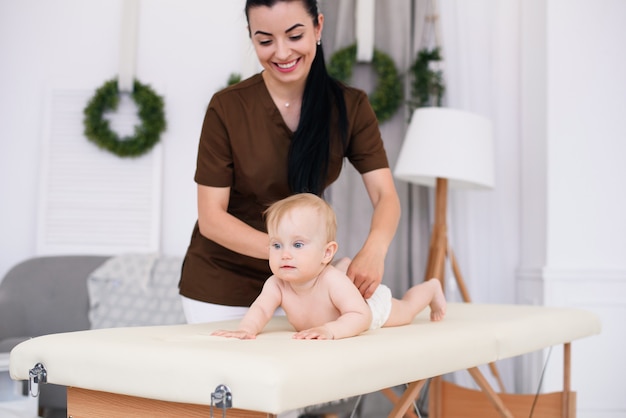 Gesundheitswesen und medizinisches Konzept. Glückliches Baby, das Massage mit professioneller Masseurin hat. Freundlicher und freundlicher Kinderarzt. Kindermassage auf der Couch in einem modernen gemütlichen Raum.