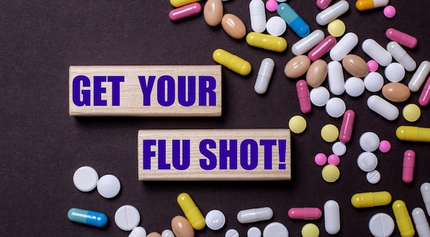 GET YOUR FLU SHOT ist auf Holzklötzen in der Nähe von mehrfarbigen Pillen geschrieben. Medizinisches Konzept