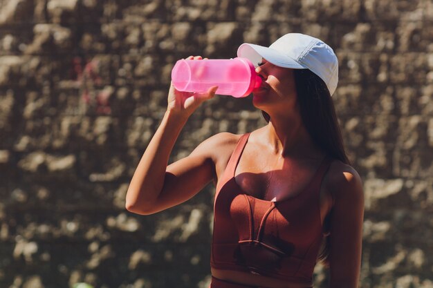 Getönten Bauch und schlanke Form der athletischen Frau, die eine Flasche Wasser hält und ein Armband trägt