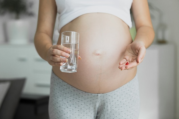 Getonte Nahaufnahme schwangere Frau mit Glas Wasser und Pillen