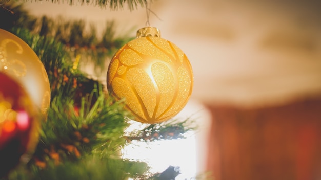 Getonter Weihnachtshintergrund. Goldene Kugeln hängen am Weihnachtsbaum gegen großes Fenster