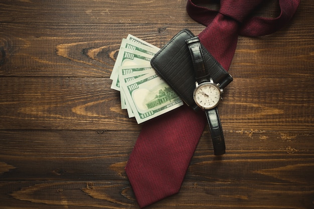 Getontes Foto von Armbanduhren, Geld im Geldbeutel und roter Krawatte auf dunklem Holzhintergrund