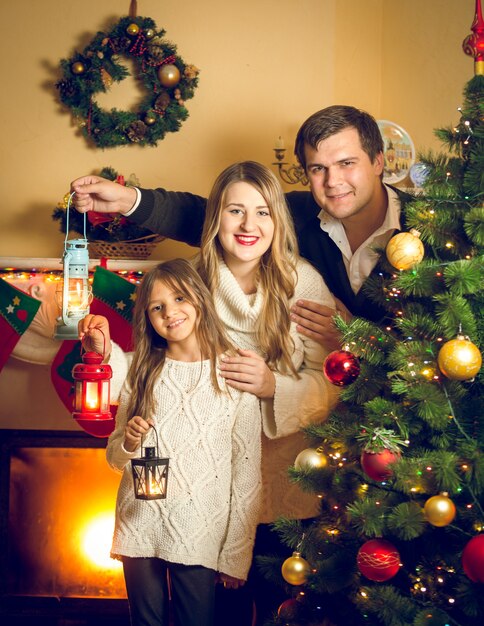 Getontes Porträt einer glücklichen Familie, die mit Laternen am Weihnachtsbaum posiert