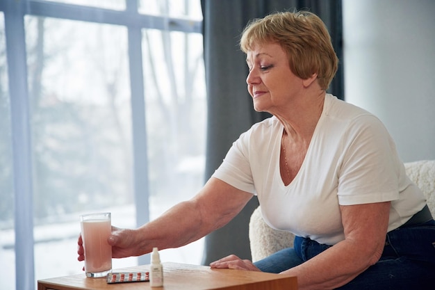 Getränk mit Anti-Grippe-Medikament Senior ältere Frau ist zu Hause im Wohnzimmer