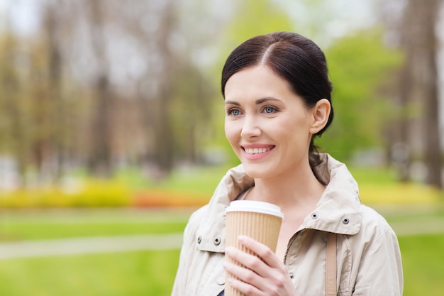 getränke, freizeit und personenkonzept - lächelnde frau, die kaffee im park trinkt
