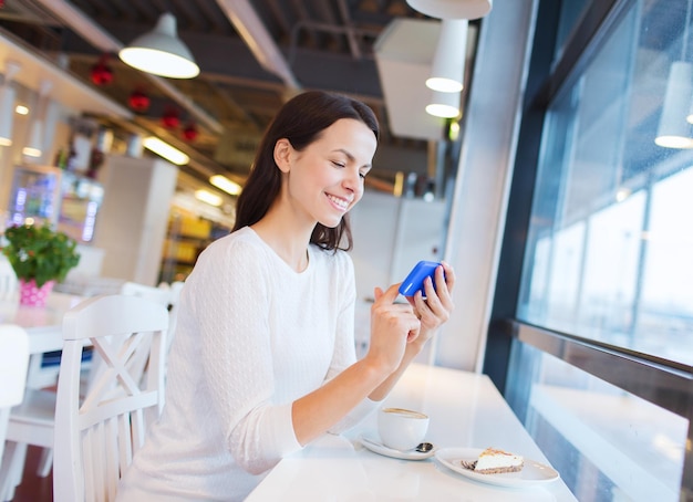 Getränke, Lebensmittel, Menschen, Technologie und Lifestyle-Konzept - lächelnde junge Frau mit Smartphone, die Kaffee im Café trinkt