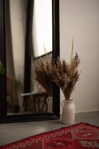 Getrocknete Blumen in einer großen Vase neben einem roten Teppich und einem Spiegel