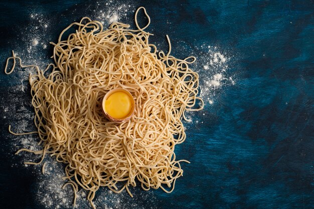 Foto getrocknete eiernudeln, rohe frische spaghettis auf blauem hölzernem hintergrund