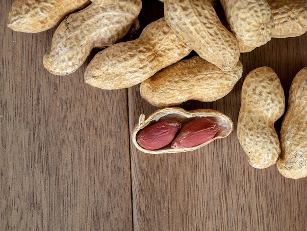 Getrocknete Erdnüsse in den Oberteilen auf Erdnusshintergrund auf Holztisch