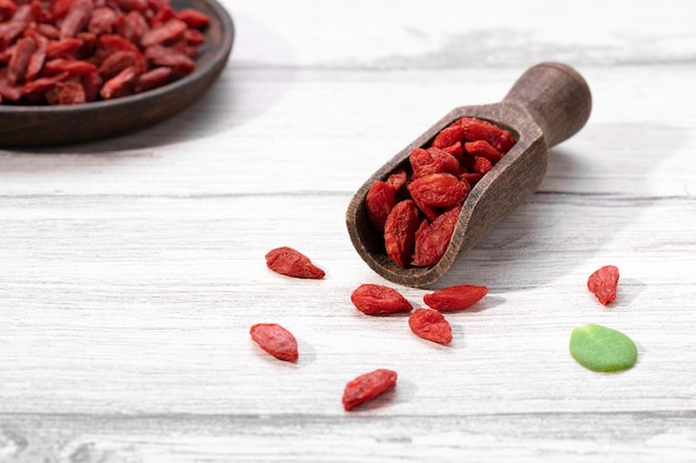 Foto getrocknete goji-beeren auf holzlöffel und holzplatte auf weißem hintergrund