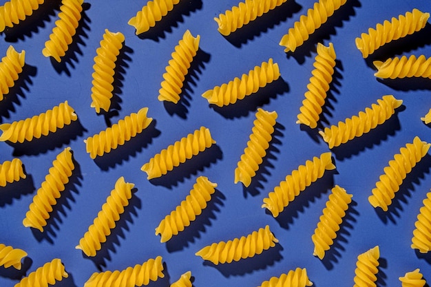 Getrocknete italienische Spiralnudeln, die auf Blau in einer Vollbild-Lebensmittel-Hintergrundtextur verstreut sind, die als flaches Stillleben angesehen wird