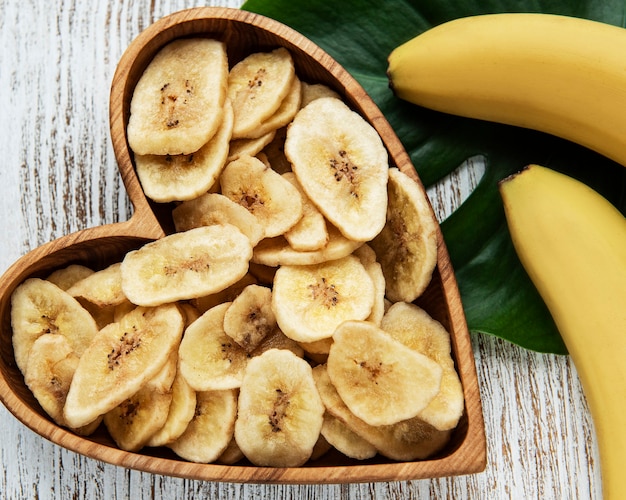 Getrocknete kandierte Bananenscheiben oder -chips auf einem weißen Holztisch