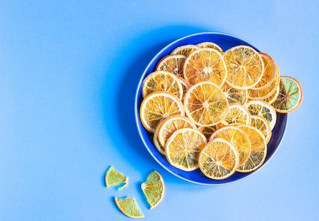 Getrocknete orange Fruchtscheiben auf einer blauen keramischen Platte, minimales Konzept der blauen Papierfrucht.